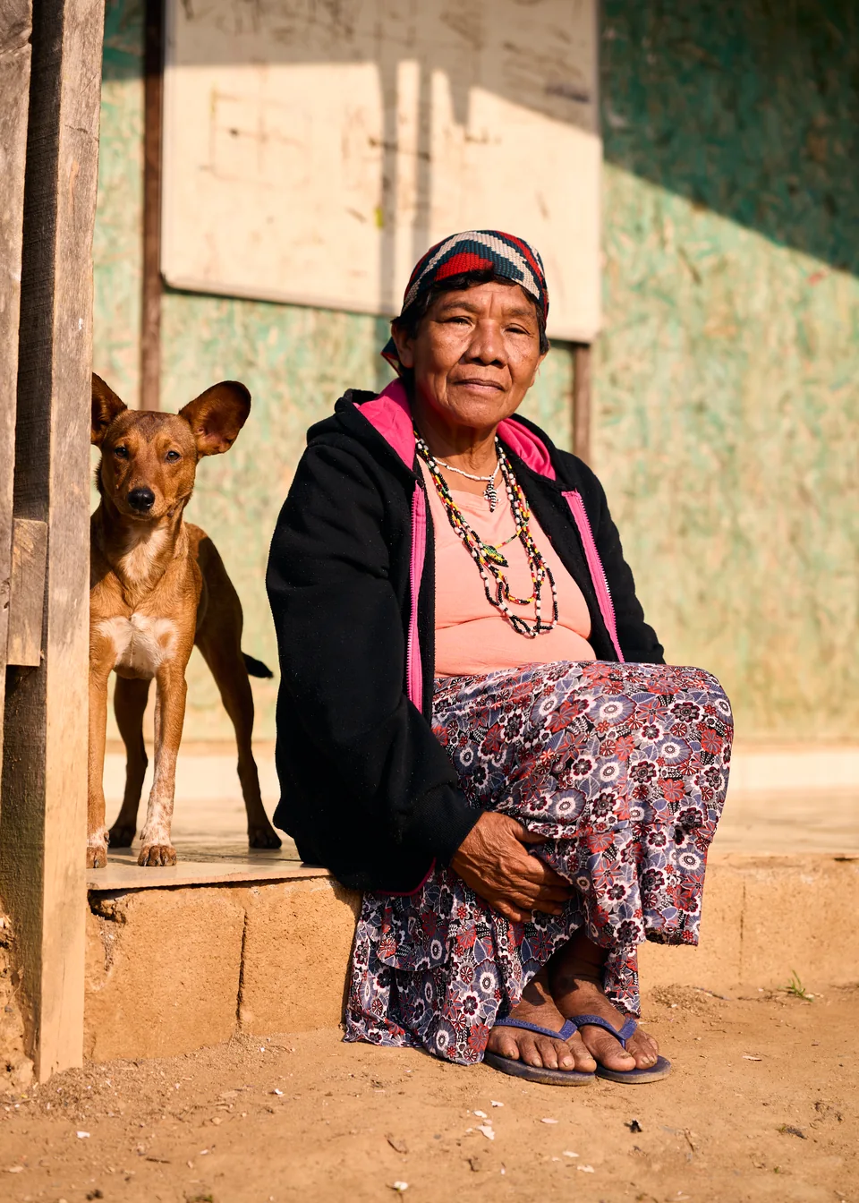 Mulher indígena com um cão junto à sua casa.