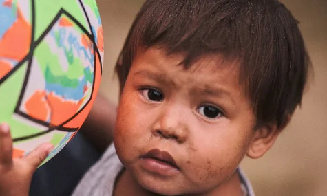 Criança pequena de cabelo castanho ao lado de uma bola colorida com estampa de mapa-múndi, em close do rosto